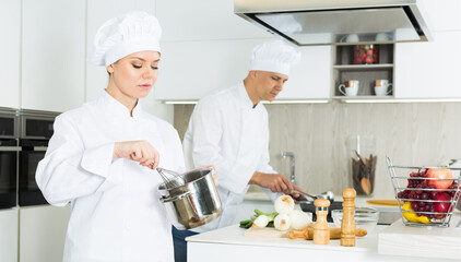 Wall Mural - Portrait of woman cook who is standing with pot for soup on her work place in the kitchen