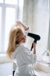 © JustLife - Beautiful woman enjoying in hotel room. Young happy smiling woman wearing bathrobe using hair dryer in bathroom.