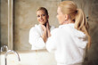 © JustLife - Beautiful woman enjoying in hotel. Young happy woman in bathrobe use the cream for the body.