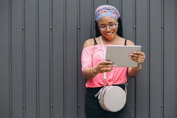 Wall Mural - Pretty young afro american woman standing and using tablet computer at the gray wall