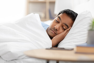 Wall Mural - people, bedtime and rest concept - sleepy indian man in bed looking at smartphone lying on table at home