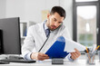 © Syda Productions - healthcare, medicine and people concept - male doctor with clipboard calling on desk phone at hospital