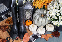 Rain Boots On The Front Porch Decorated For Autumn With Heirloom Gourds,  White Pumpkins, Mums And Buffalo Plaid Welcome Mat For An Inviting Atmosphere.