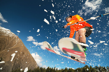 man skier in flight after jumping from a kicker in the spring against the backdrop of mountains and blue sky. Close-up wide angle. The concept of closing the ski season and skiing in spring