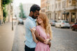 © MZaitsev - Interracial Relations. An African man and a Caucasian woman stand embracing on a city street.