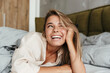 © Drobot Dean - Image of woman laughing and winking at camera while lying in bed