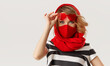 Woman in trendy fashion outfit during quarantine of coronavirus outbreak. Model in protective stylish red face mask and heart shape sunglasses on white background