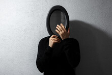Dramatic Portrait Of Young Man With Black Oval Mirror On Face. Textured Abstract Background Of Grey Wall.