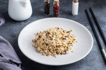 Brown and unpeeled rice on a plate with chopsticks. Dark concrete background. Copy space.