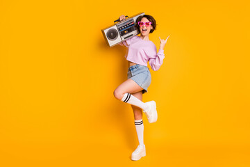 Poster - Full length body size view of nice attractive funny cheerful cheery excited glad girl carrying boombox having fun dancing showing horn sign isolated bright vivid shine vibrant yellow color background