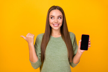 Sticker - Portrait of positive cheerful excited girl promoter hold smartphone point forefinger copyspace advise shop she buy new device wear sweater isolated over shine color background