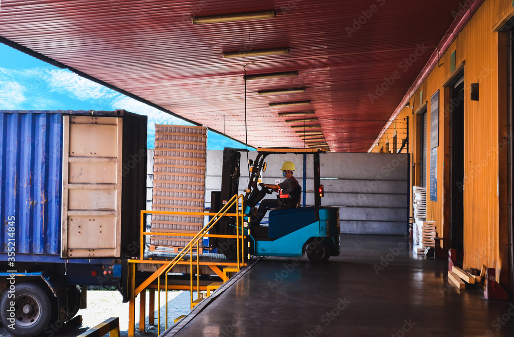 Forklift stuffing-unstuffing pallets of cargo to container on warehouse leveler dock. - obrazy, fototapety, plakaty 