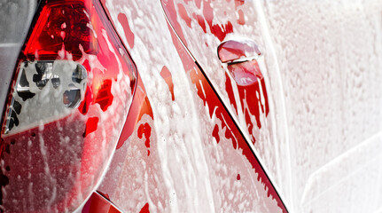 Manual car wash cleaning with foam and pressured water at service station outdoor