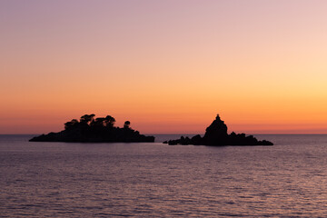 Two islets off Petrovac Montengro, on the coast of the Adriatic sea (Katic and Sveta Nedjelja - Saint Sunday). Silhouette of the famous landmark against colorful orange and purple sunset sky.