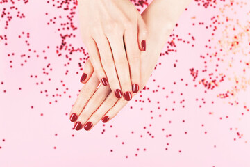 Wall Mural - Manicure and nailcare concept. Two woman hands and falling confetti on pink background. Flat-lay, top view. Copy space.