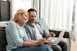 © LIGHTFIELD STUDIOS - Smiling mature couple using laptop and credit card on couch
