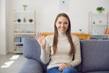 Young woman looking at the camera waving her hand online while having a laptop of call connection with a virtual man in the room.