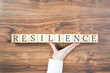 Resilience word on wooden building blocks with supporting hand. Recovering and building resilience concept, coping with crisis. Copy space