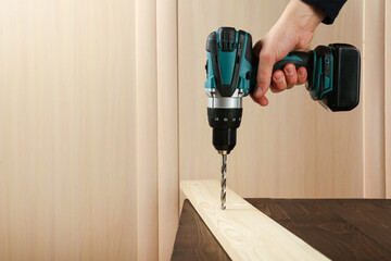 Sticker - carpenter's hand is drilling wood plank by cordless drill close up with copy space