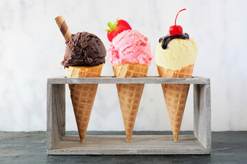 Wall Mural - Ice cream cone assortment in waffle cones against a white marble background. Chocolate, strawberry and vanilla flavors with toppings.