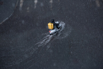 Motorcyclist rides on a flooded street with a yellow backpack on his back