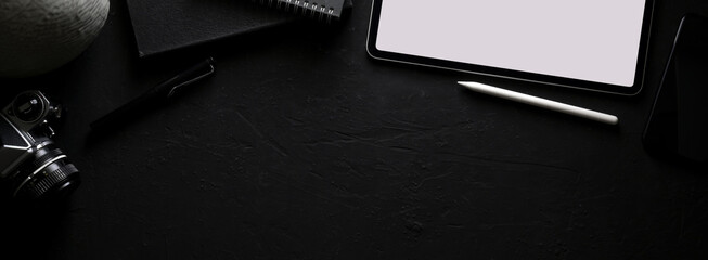 Dark modern workspace with blank screen tablet, stationery, camera and copy space on black table