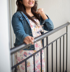 Wall Mural - Half face portrait of an Indian Bengali beautiful and cute brunette girl in a casual blue jeans shirt and white top is standing on a balcony with black grills. Indian lifestyle and fashion portrait