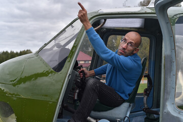 Beautiful portrait of a brutal man in glasses, a guy, a brunette, with stubble, sitting in a small helicopter on nature on a summer day.