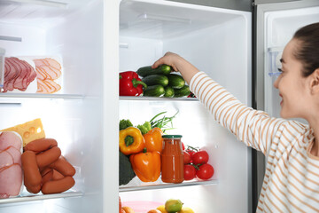 Canvas Print - Young woman taking cucumber out of refrigerator, closeup