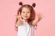 © oes - Portrait of surprised cute little toddler girl child over pink background. Looking at camera. Points hands to the left side. Advertising childrens products