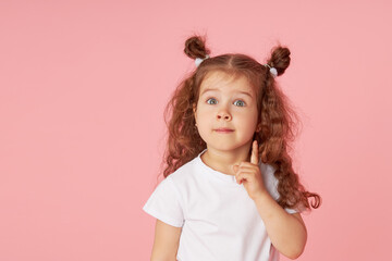 portrait of surprised cute little toddler girl child over pink background. looking at camera. points