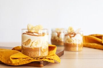 homemade banoffee pie in a glass cup on wooden table background.