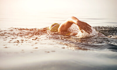 Unknown triathlon swimmer at sea. athletic young woman swimming freestyle in morning open water