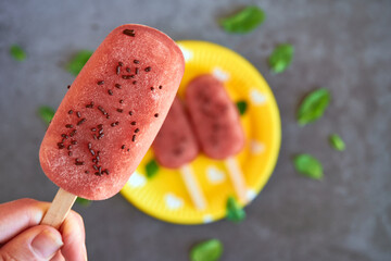 Holding sweet frozen watermelon with lime and mint popsicle, great for kids and adults in the summertime homemade popsicles with chocolate sprinkles on a yellow paper plate with hearts in background