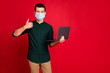 © deagreez - Portrait of his he nice attractive guy wearing safety mask using laptop showing thumbup stop cov ncov influenza infection prevention isolated bright vivid shine vibrant red color background