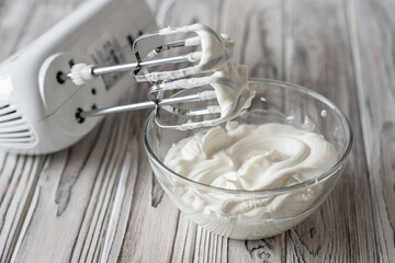 Woman whipping cream using electric hand mixer on the gray rustic wooden table