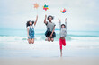 © Stella - Cute groups of kids have fun on sandy summer beach with blue sea, happy childhood friends  jump together and play on tropical beach,  children raise hand up, hold ball and paper windmill