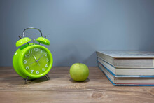 Green Clock,green Apple And A Bunch Of Books In Grey Background.Time And Health Concept 
