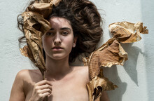 Portrait Of A Young Sexy Woman With Brown Hair Artfully Decorated Between Leaves Of Dry, Withered Banana Tree Looking Like An Art Nouveau Girl, Copy Space.