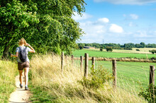 Woman Hiking On Footpath By Agricultural Fields. Photo Taken On The Cotswold Way In Gloucestershire, England