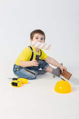 Wall Mural - a small boy in a Builder's suit makes repairs on a white background