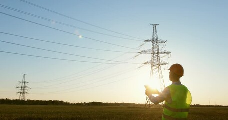 Wall Mural - an energy engineer in special clothes inspects a power line using data from electric sensors on a ta