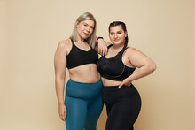 Body Positive. Plus Size Models Portrait. Confident Full-Figured Women In Sport Clothes Against Beige Background. Fitness For Active Lifestyle.