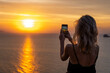 © Volodymyr_sh - Woman hands holding mobile phone at sunset. Young curly hair woman taking photos with her cell phone in a beautiful amazing sunset over sea. Taking a picture on a smartphone during a vacation
