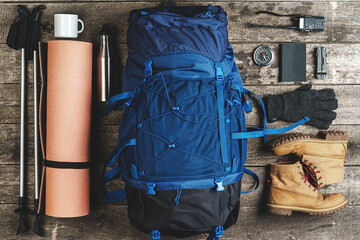backpack and hiking equipment on wooden background, top view