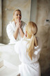 © JustLife - Beautiful woman in bathrobe use the cream for the body. Young woman enjoying in hotel.