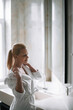 © JustLife - Beautiful woman in bathrobe use the cream for the body. Young woman enjoying in hotel.