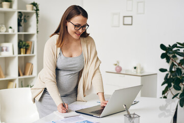 Canvas Print - Pregnant businesswoman in smart casualwear bending over desk by laptop