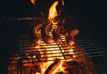 Cooking a sausages meat on barbecue. Four sausages on grill. Concept of eating outdoor at country house backyard during summer time .