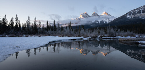 Wall Mural - Panoramic winter sunrise shot from Canadian Rockies with mountain reflected in water, shot at Three Sisters Mountain, Canmore, Alberta, Canada